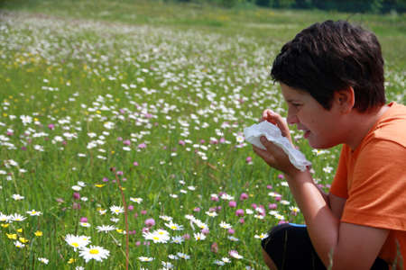 allergic child to pollen and flowers with a handkerchief while sneeze in the middle of meadowの写真素材