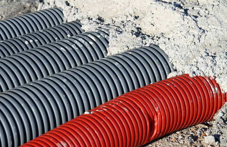 Red pvc corrugated hose and four gray pipes for laying electric cables and optical fiber in a...