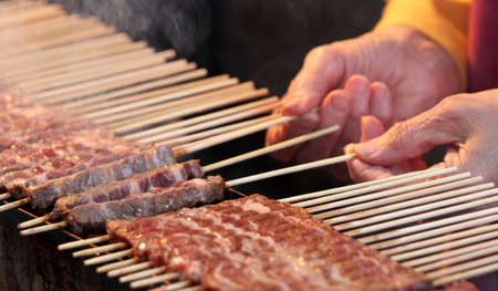 hand while turning the skewers of cooked meat sold at the marketの写真素材
