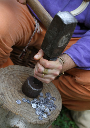 medieval craftsman while coins coins of lead and silver with huge hammer and punch