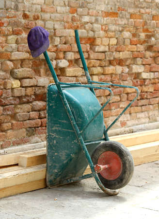 Wheelbarrow laid on the wall and worker's Capの写真素材