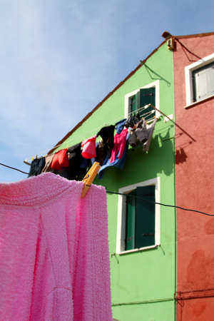 Pink cotton Bathrobe laid out to dry and the colorful houses on the island of Buranoの写真素材