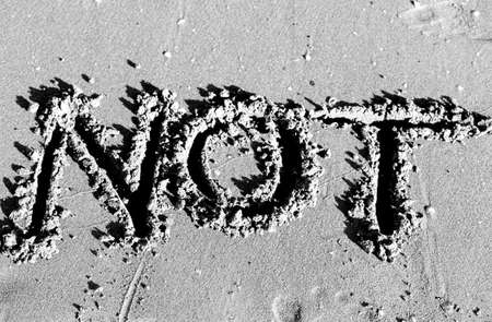 written NOT designed on the sand of the beach in black and whiteの写真素材