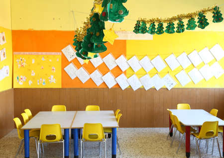 kindergarten classroom with yellow chairs and table with drawings of children hanging on the wallsの写真素材
