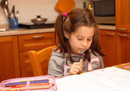 young girl writes with pencil on the school book in the kitchen