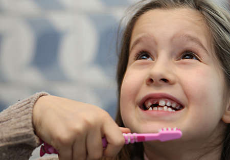 young girl without a tooth while brushing teeth in the bathroomの写真素材