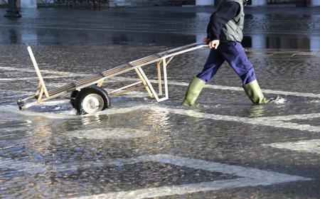 Venice Worker with the transport cart and green boots at high tide