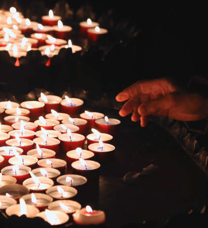 hand of an elderly woman lights a candle to pray during mass at Churchの写真素材