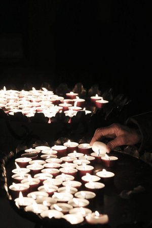 hand of an elderly woman lights a candle to pray during mass at Church