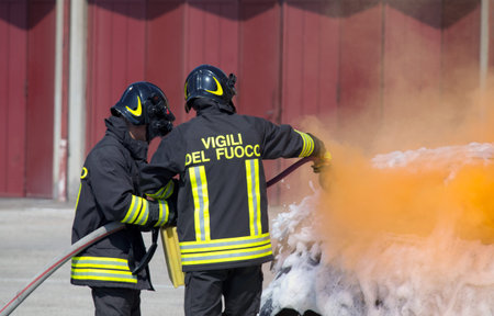 two firefighters in action with foam to put out the fire of the car