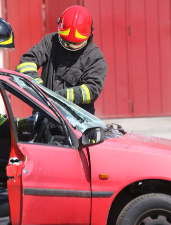 chief fireman whit red helmet while breaking the windshield of a car after traffic accidentの写真素材
