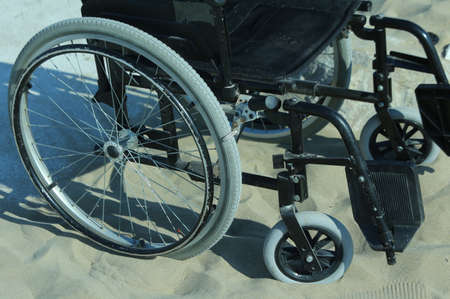 black wheelchair stuck in the sand on the seashoreの写真素材