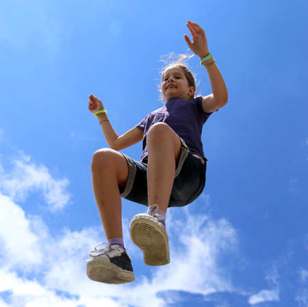 cheerful little girl makes a big jump and blue sky in summerの写真素材