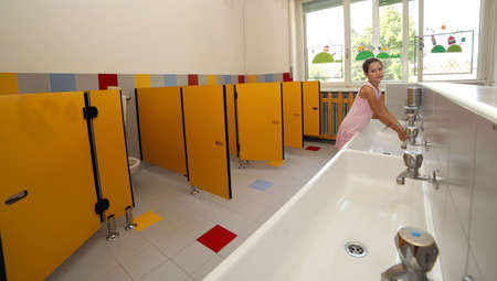 smiling girl washing her hands in the sink in the bathroom of the schoolの写真素材