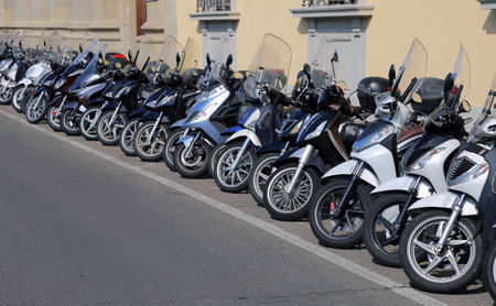 many mopeds scooters and motorcycles parked along the busy street