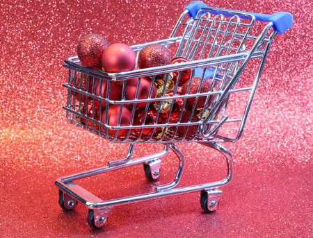 mini shopping cart with red decorative Christmas balls and glitter backgroundの写真素材