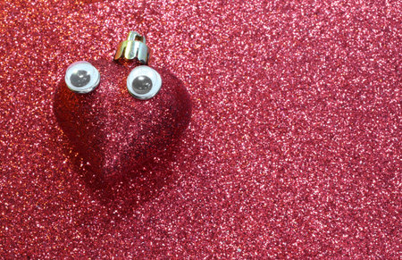 lone red heart with big sad languid eyes on  shiny red backgroundの写真素材