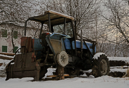 abandoned tractor without a wheel in the snow in winterの写真素材