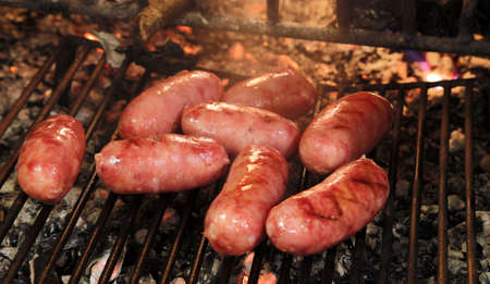 big and fat pork sausages on the grill of the fireplace with fire burningの写真素材