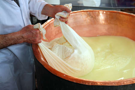 Senior expert cheesemaker collects the cheese with the tarp from the large copper cauldron filled with milk and wheyの写真素材