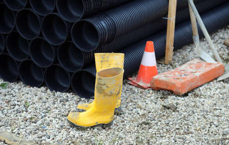 Yellow rubber boots with a traffic Cone and black plastic tubes in road constructionの写真素材