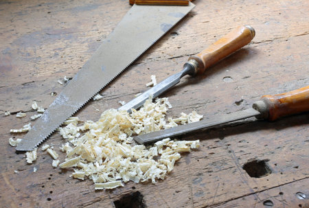 two chisels and a hand saw with wood shavings in the Workbench with a wooden vise inside the...