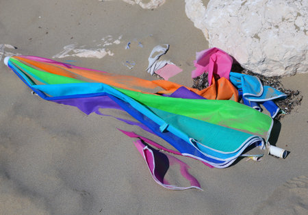 broken colored parasol at the sandy beach after summer holidaysの写真素材
