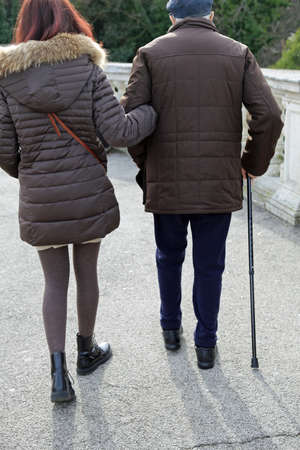 young woman accompanies the older gentleman with walking stickの写真素材