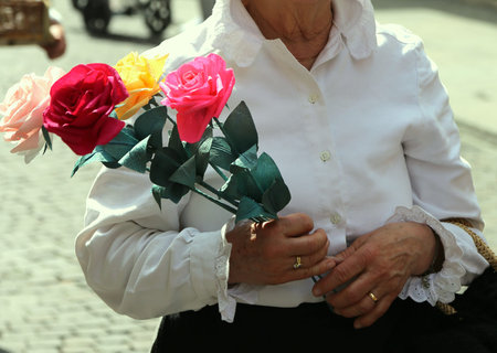 old lady with white blouse walks with a pack of four roses in her hand