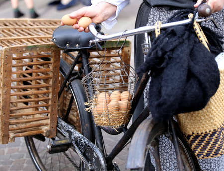elderly woman on bike with two eggs in hand and many hen eggs in the basketの写真素材