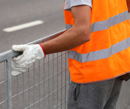 worker with high visibility reflective jacket moves iron hurdles before the sporting event on the roadの写真素材