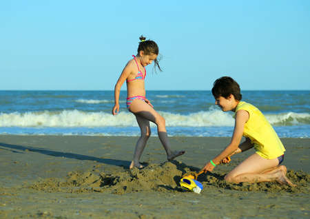 lovely little girl and her brother play with sand in the beach in summerの写真素材