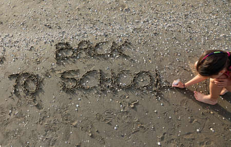 little girl writes the phrase Back to School on the beachの写真素材