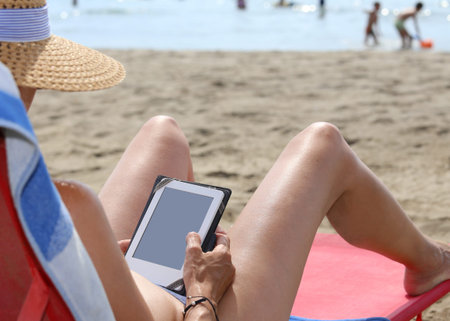 long legs of a beautiful girl while reading an ebook on the Beach in summerの写真素材