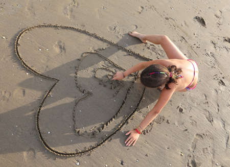 little girl draws many hearts on the beach in summerの写真素材