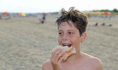 nice guy while eating a big sandwich on the beach in summerの写真素材