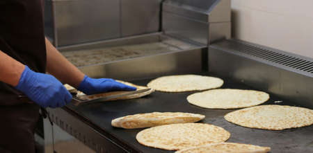 experienced cook with latex blue gloves cooking Italian tpical dish called piadina romagnola on the hot plateの写真素材