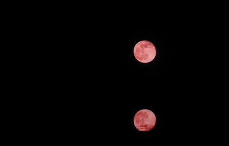 fantastic full red moon with reflection in water on a dark night with no starsの写真素材