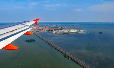 wing of a passenger jet over the very long bridge of freedom to the island of Venice in Italyの写真素材