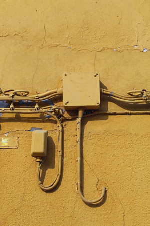 old yellow wall of the house and the junction box with the electric and telephone cablesの写真素材