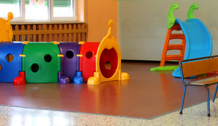 a tunnel shape game and a slide in the large hall of kindergarten without peopleの写真素材