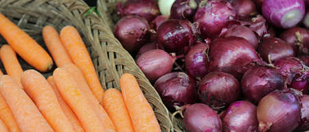 basket of orange carrots and red onions for sale at the greengrocerの写真素材