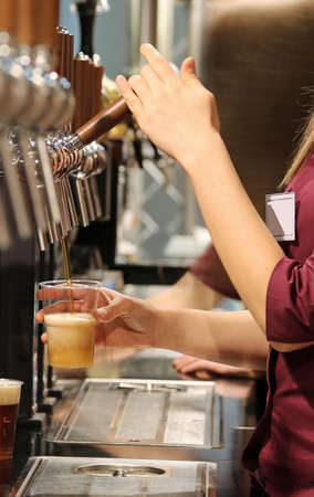 waitress fill the bush of cold beer in the barの写真素材