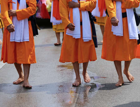 many men of Sikh Religion with long orange clothes walk barefoot with swords in hand on the paved roadの写真素材