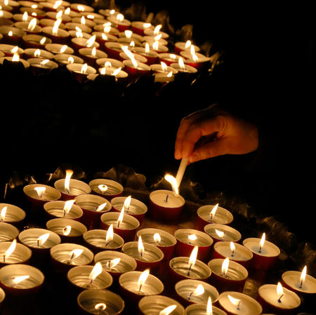 hands of an elderly woman who lights a candle during the Holy Mass in the Christian church and many...