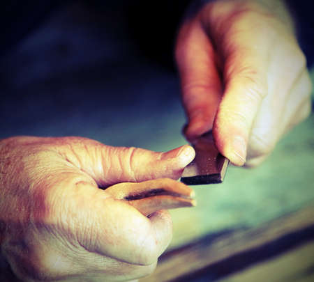hands of an elderly carpenter while the piece of wood with a sharp chiselの写真素材