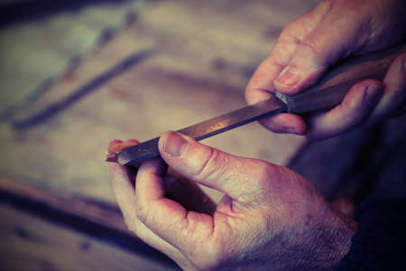 hands of an elderly carpenter while the piece of wood with a sharp chiselの写真素材
