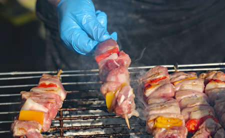 blue glove of cook and hot skewers when cooking on the grill in the food stall on the streetの写真素材