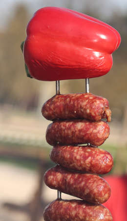 skewer with red peppers and succulent pork sausages on a spit in the street stallの写真素材