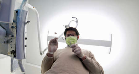 Man with mask and tools and white latex gloves for oral cleaning in a dental studioの写真素材